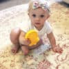 A baby playing with a yellow toy on a rug.