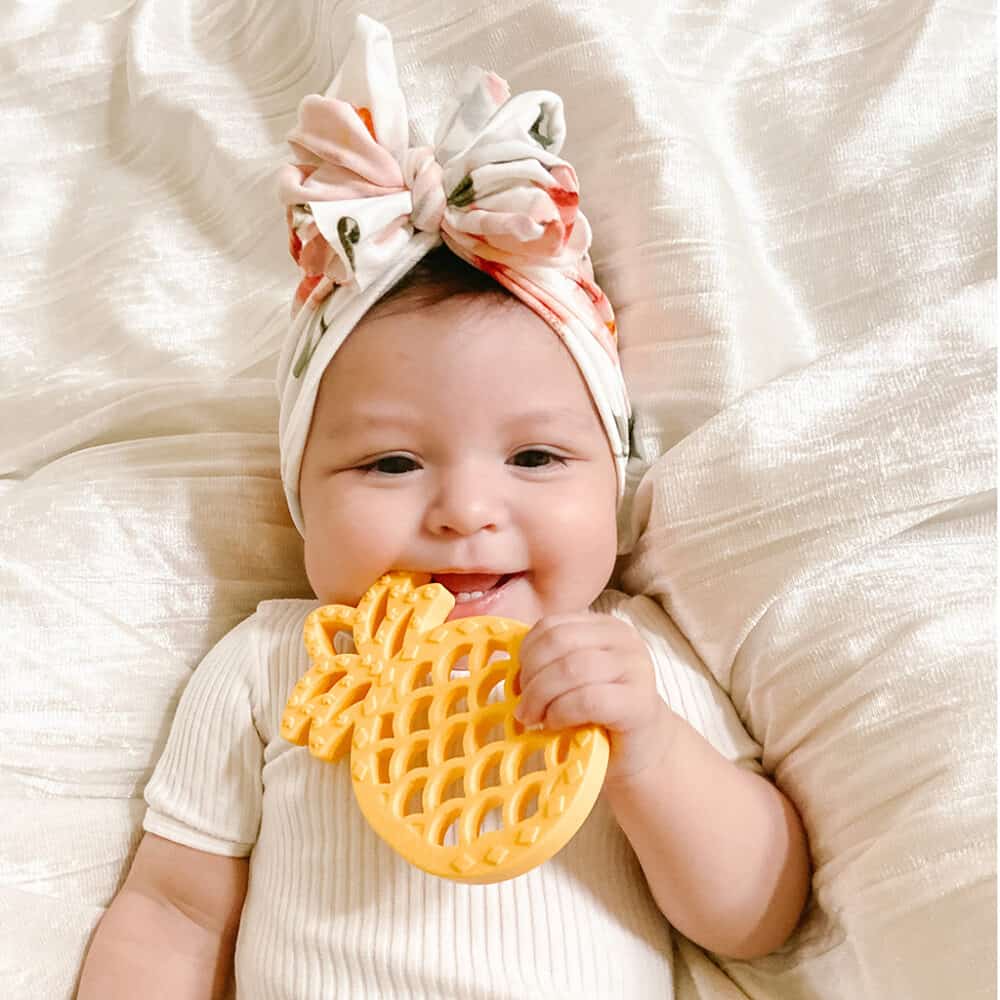 A baby wearing a headband holding a pineapple toy.