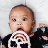 A baby is laying on a bed with a toy in her mouth.