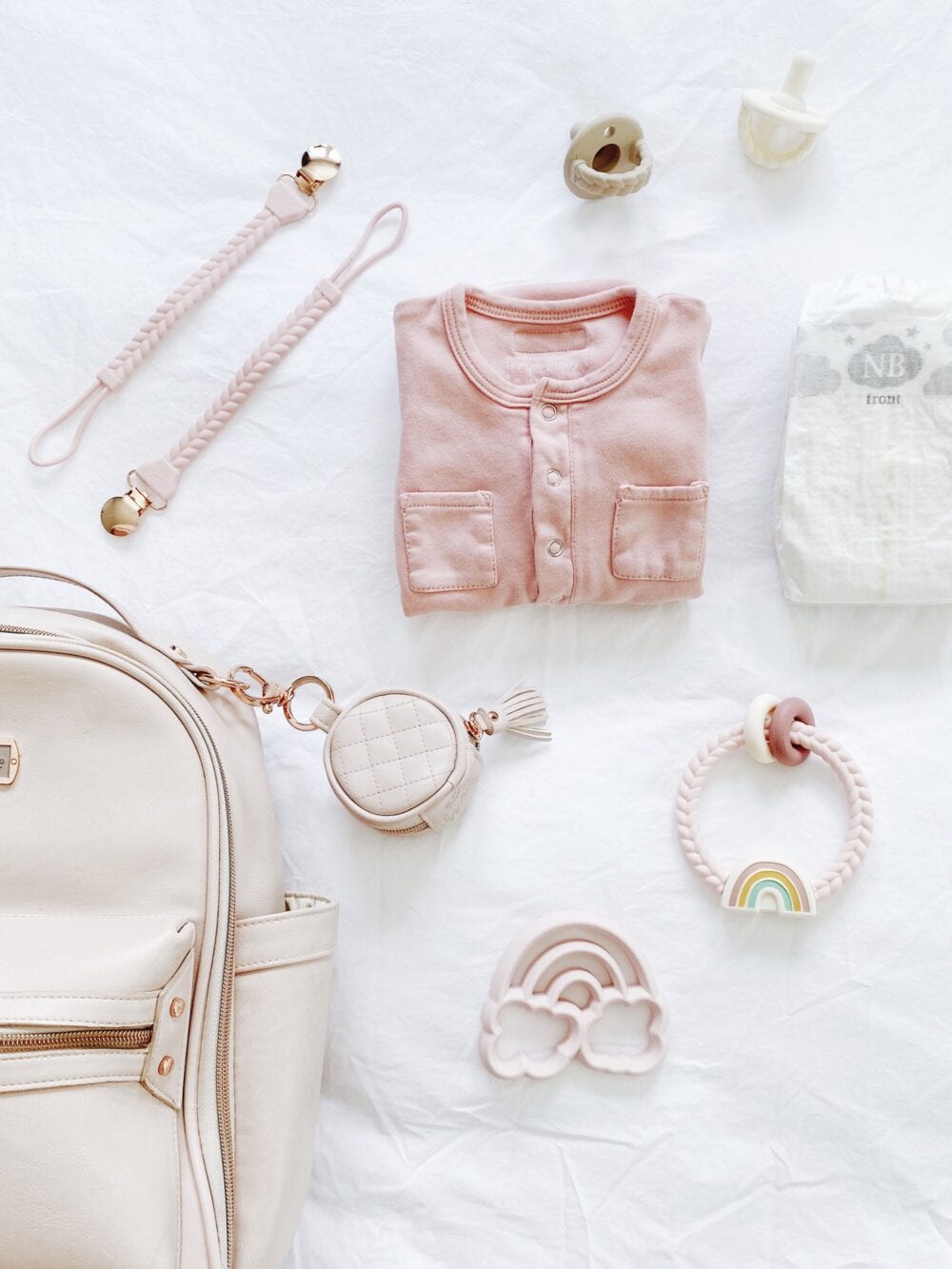 A pink baby bag and other baby items laid out on a bed.