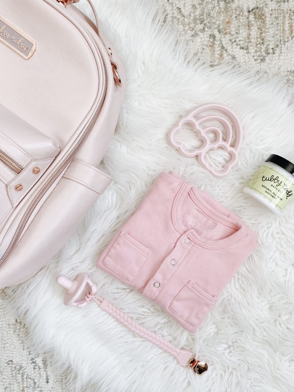 A pink diaper bag with baby items on a white fur rug.