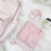 A pink diaper bag with baby items on a white fur rug.