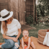 A woman with a baby sitting on a picnic blanket.