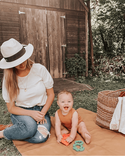 A woman with a baby sitting on a picnic blanket.