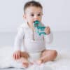 A baby is sitting on a white rug with a toy in his mouth.