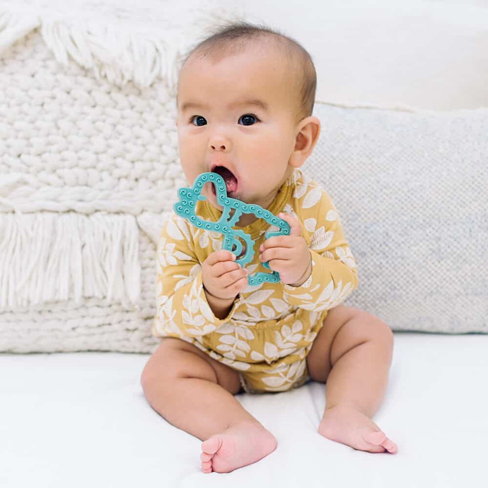 A baby is sitting on a bed eating a toy.