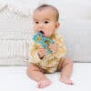 A baby is sitting on a bed eating a toy.