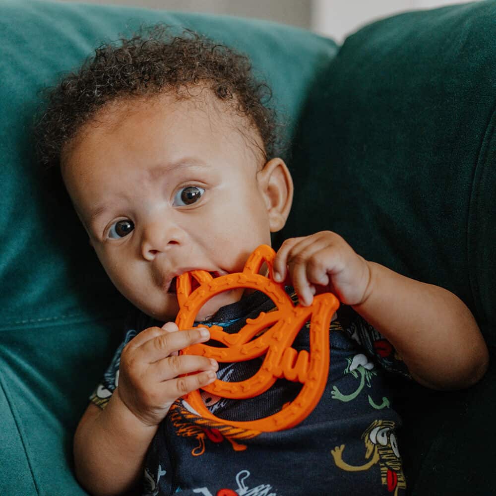 A baby is chewing on an orange toy.