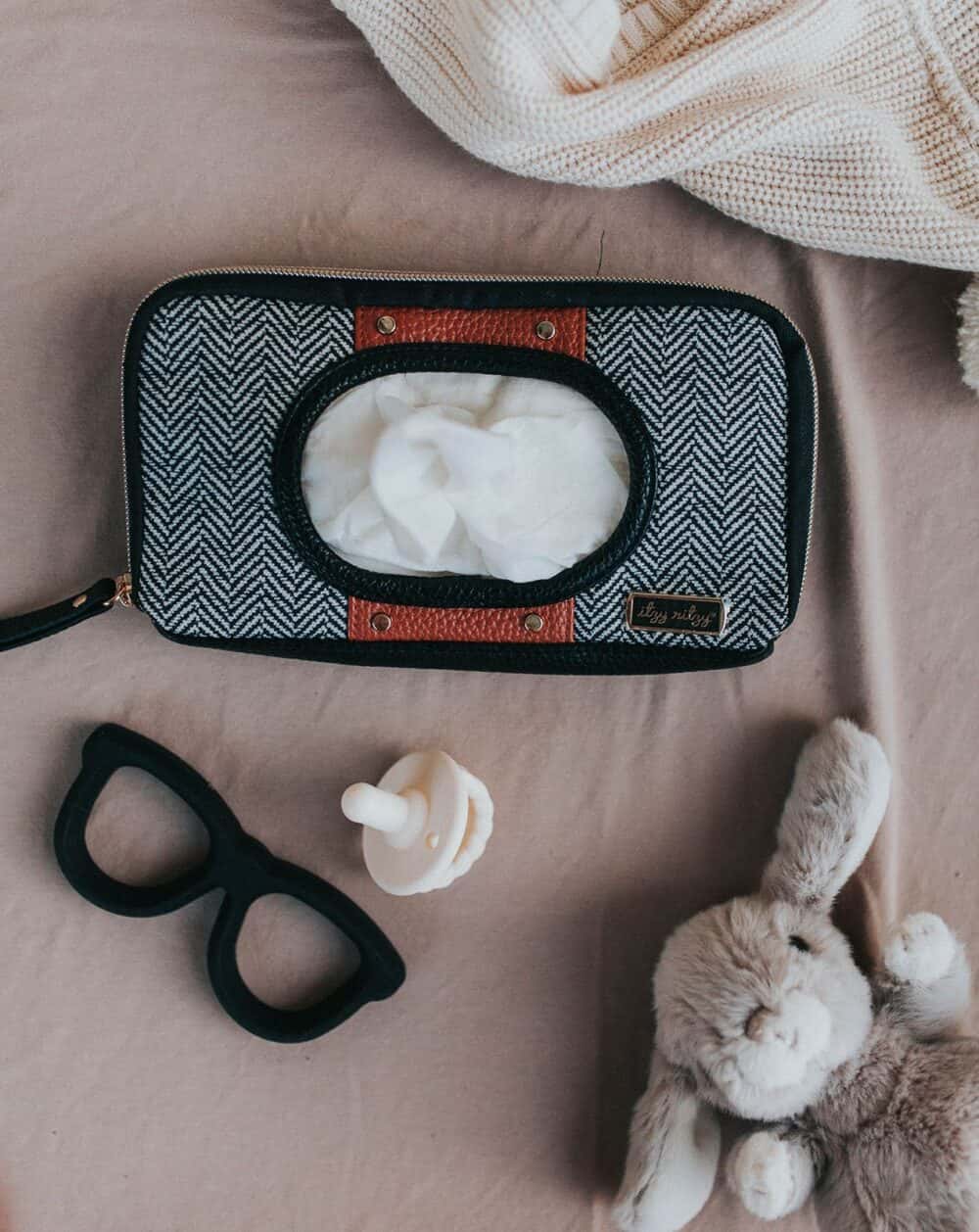 A teddy bear, glasses and a Chew Crew Silicone Baby Teether on a bed.