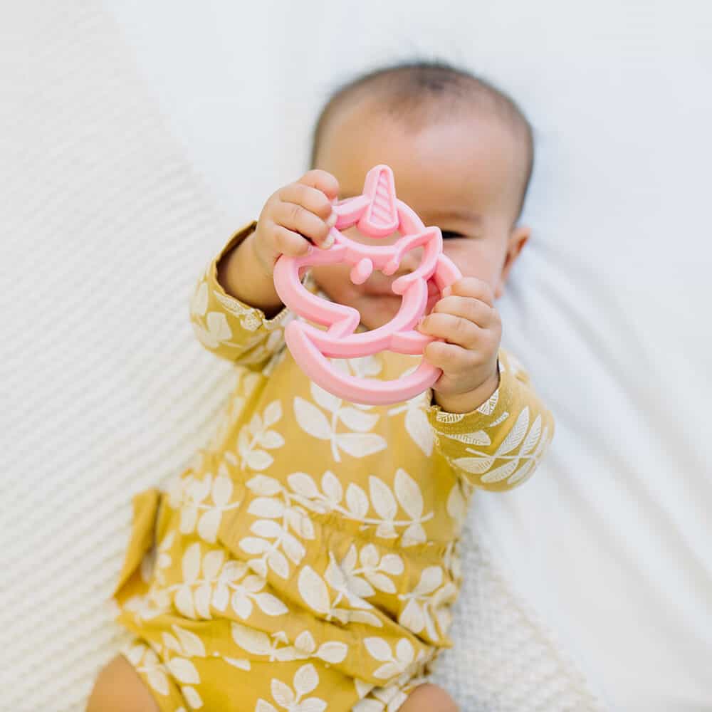 A baby is playing with a pink unicorn toothpick.