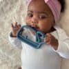 A baby is laying on a blanket with a toy in her mouth.