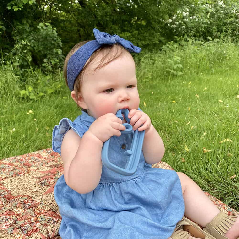 A baby is sitting on a blanket eating a toy.