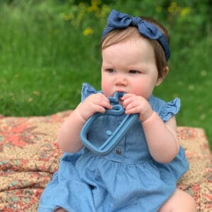 A baby is sitting on a blanket eating a toy.