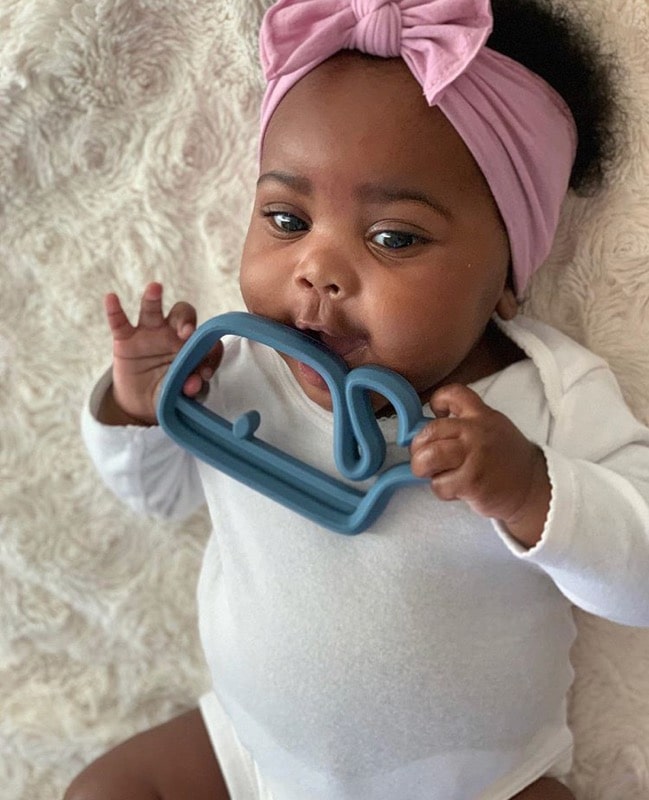 A baby is laying on a blanket with a toy in her mouth.