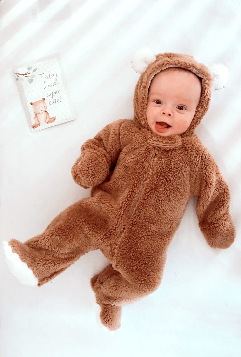 A baby in a bear costume laying on a bed.