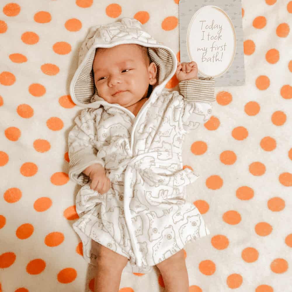 A baby in a hooded robe laying on a polka dot blanket.