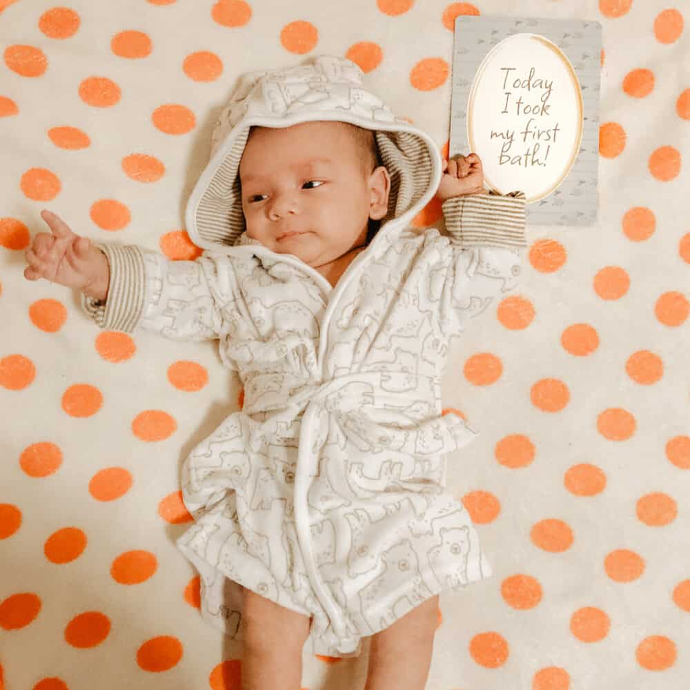 A baby in a hooded robe laying on a polka dot blanket.