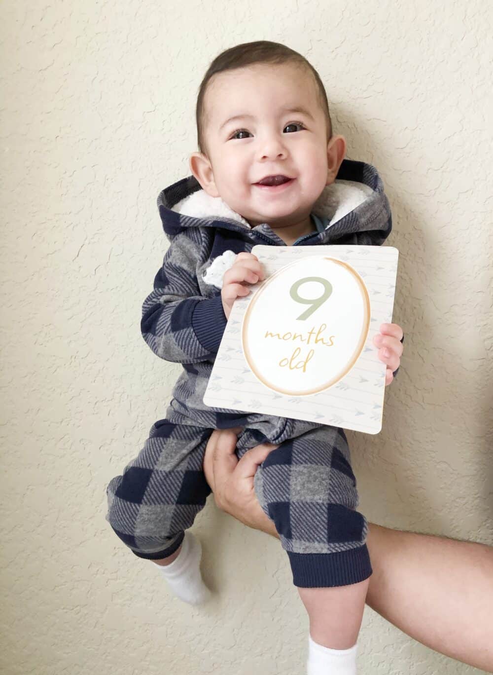 A baby is holding up a sign with the number 9 on it.
