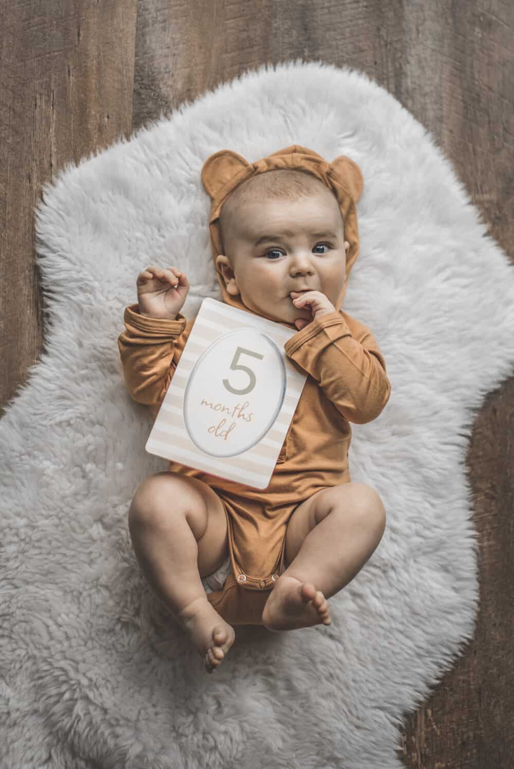 A baby wearing a teddy bear holding a number sign.