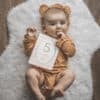 A baby wearing a teddy bear holding a number sign.