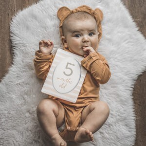 A baby wearing a teddy bear holding a number sign.