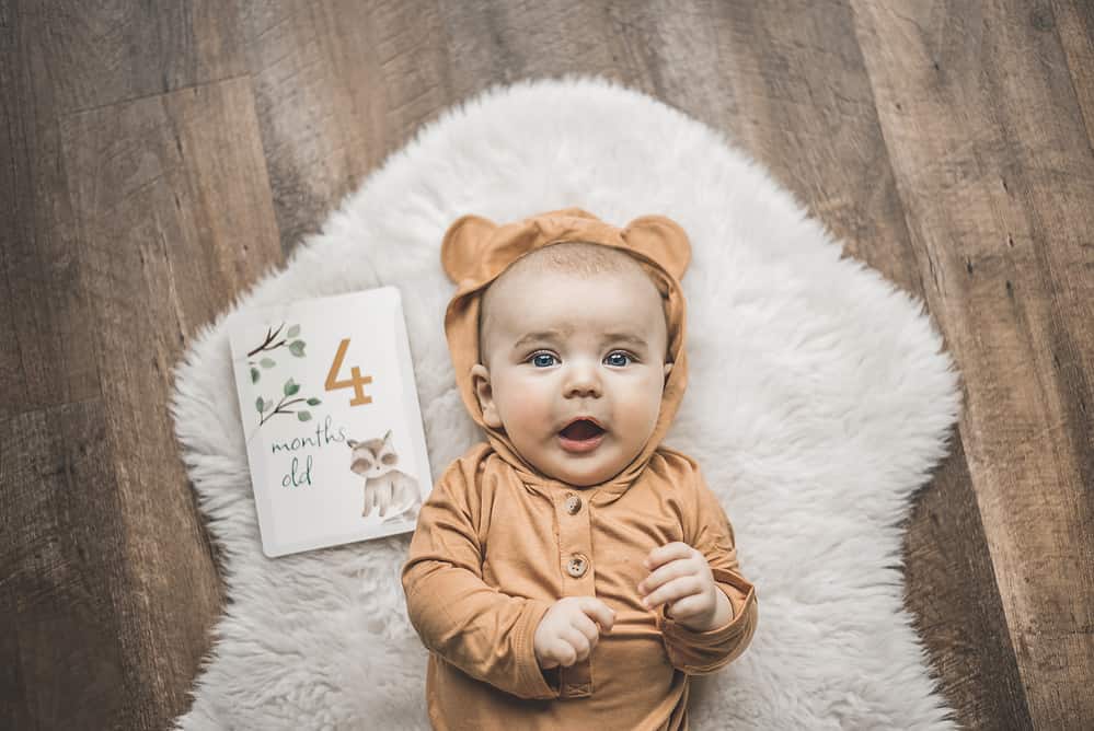 A baby laying on a rug with a book and a teddy bear.