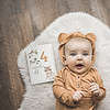 A baby laying on a rug with a book and a teddy bear.
