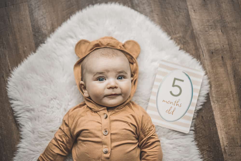 A baby in a teddy bear outfit laying on a rug.