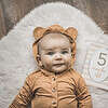 A baby in a teddy bear outfit laying on a rug.