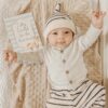 A baby is laying on a blanket and holding a card.