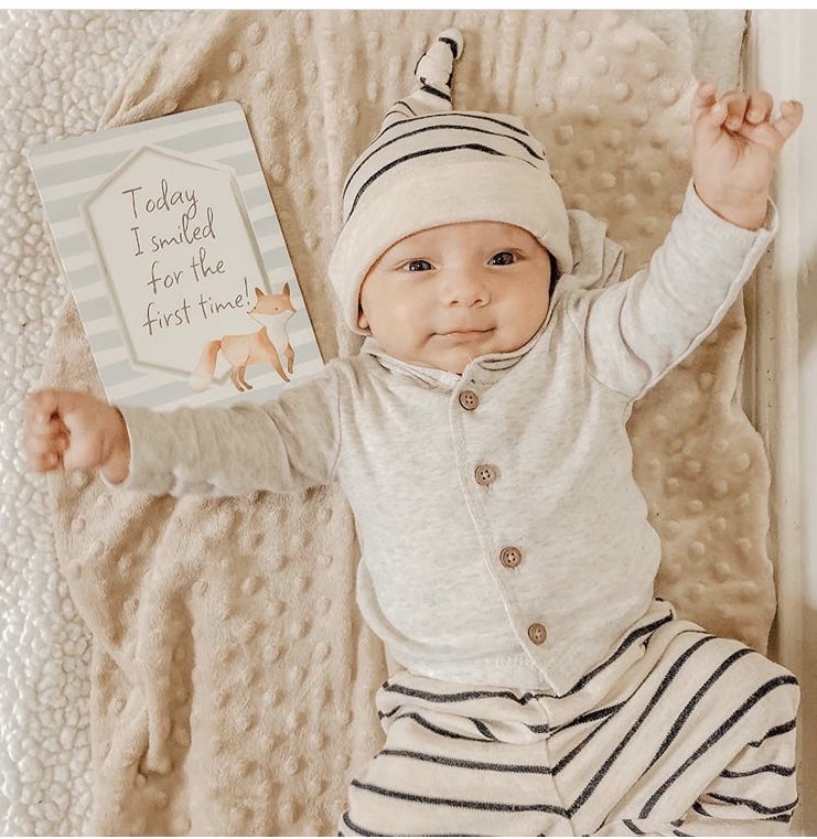 A baby is laying on a blanket and holding a card.