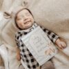 A baby laying on a blanket with a sign.