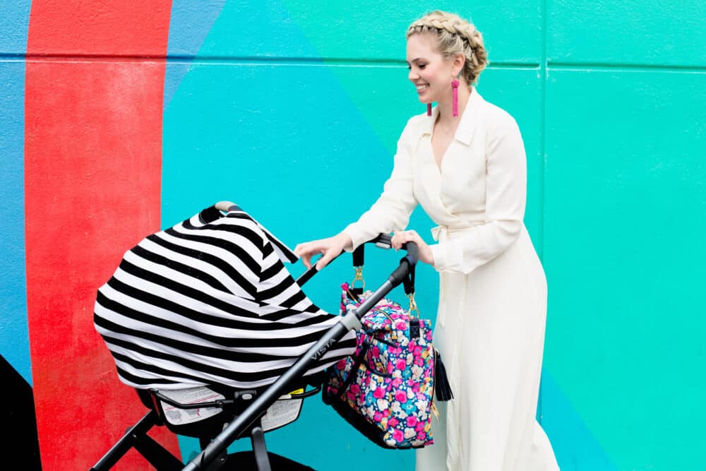 A woman pushing a Mom Boss™ 4-IN-1 Multi-Use Nursing Cover & Scarf in front of a colorful wall.