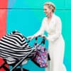 A woman pushing a Mom Boss™ 4-IN-1 Multi-Use Nursing Cover & Scarf in front of a colorful wall.
