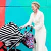 A woman pushing a Mom Boss™ 4-IN-1 Multi-Use Nursing Cover & Scarf in front of a colorful wall.