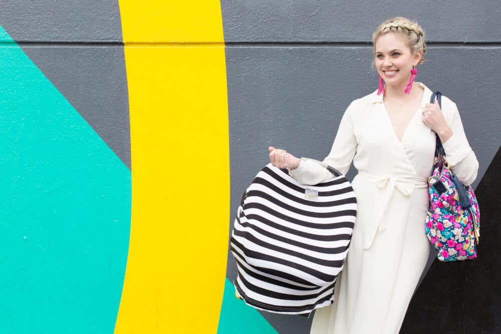 A woman in a white dress standing next to the Mom Boss™ 4-IN-1 Multi-Use Nursing Cover & Scarf.