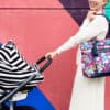 A woman standing in front of a colorful wall with a Mom Boss™ 4-IN-1 Multi-Use Nursing Cover & Scarf.