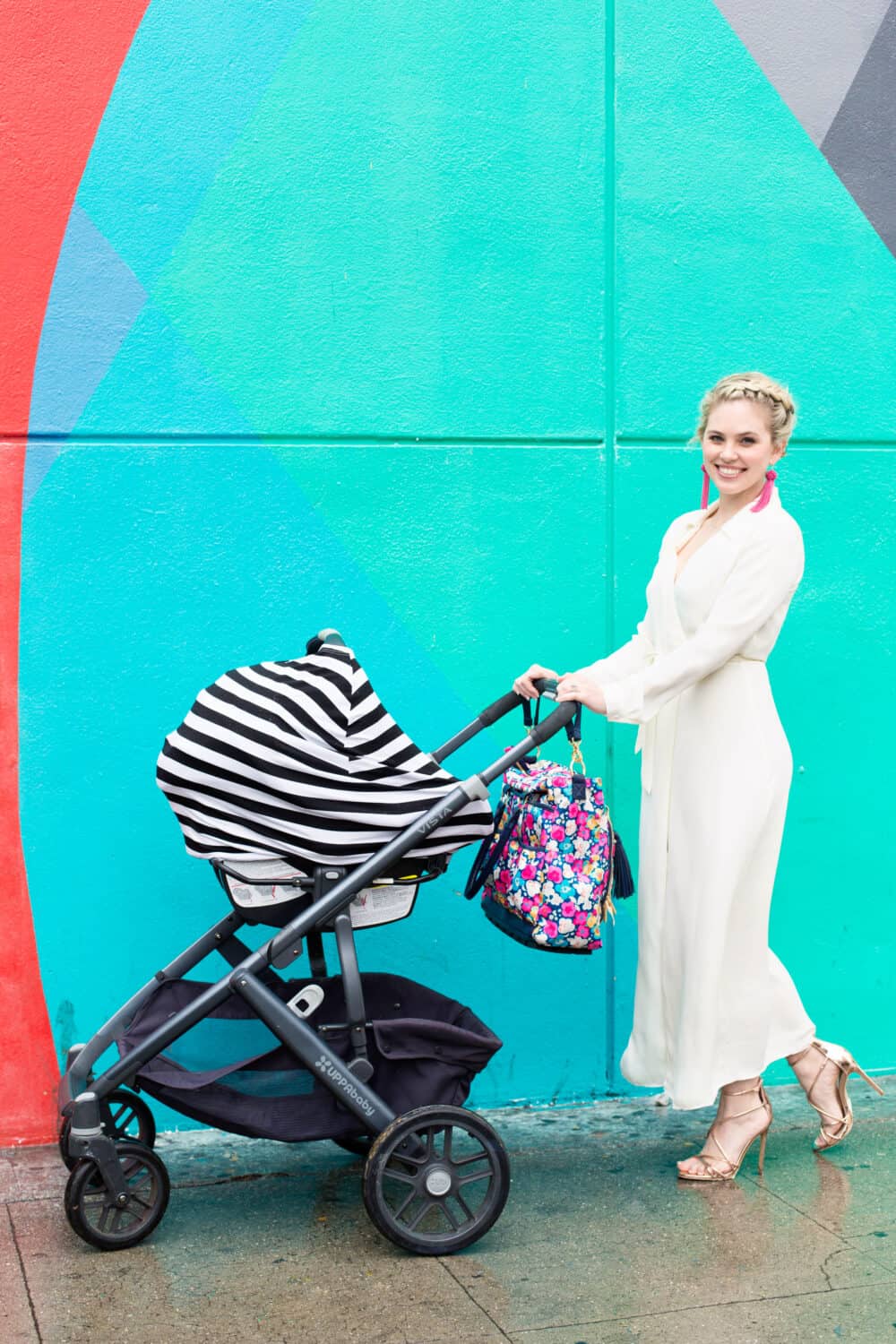 A woman pushing a Mom Boss™ 4-IN-1 Multi-Use Nursing Cover & Scarf in front of a colorful wall.