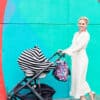 A woman pushing a Mom Boss™ 4-IN-1 Multi-Use Nursing Cover & Scarf in front of a colorful wall.