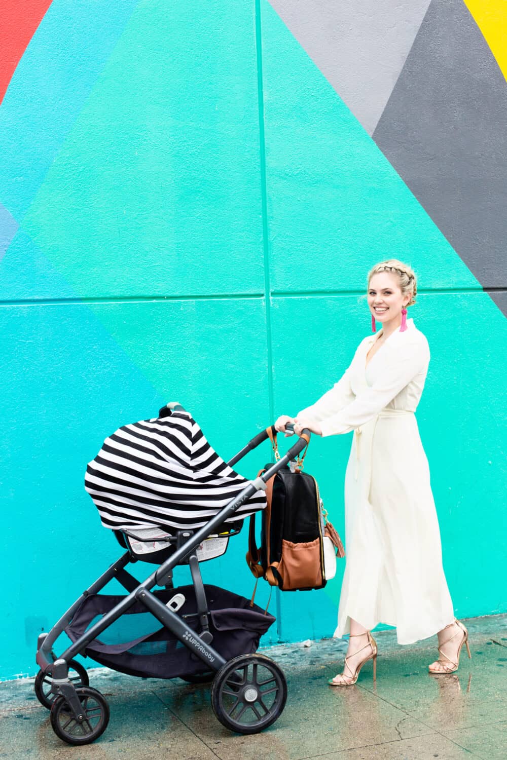 A woman pushing a Mom Boss™ 4-IN-1 Multi-Use Nursing Cover & Scarf in front of a colorful wall.