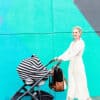 A woman pushing a Mom Boss™ 4-IN-1 Multi-Use Nursing Cover & Scarf in front of a colorful wall.