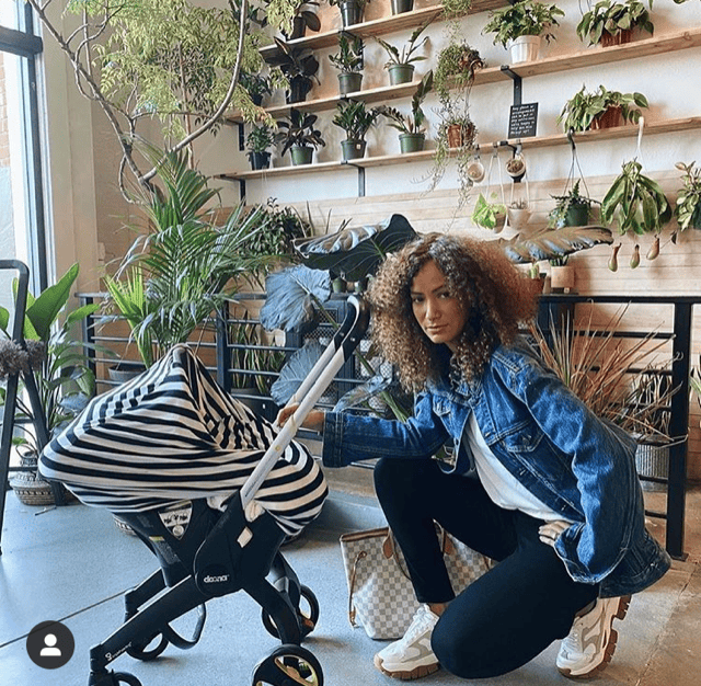 A woman kneeling in front of a Mom Boss™ 4-IN-1 Multi-Use Nursing Cover & Scarf zebra print stroller.