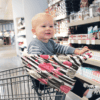 A baby sitting in a Mom Boss™ 4-IN-1 Multi-Use Nursing Cover & Scarf in a grocery store.