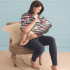 A woman is sitting on a chair holding a Mom Boss™ 4-IN-1 Multi-Use Nursing Cover & Scarf.