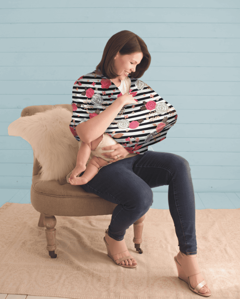 A woman is sitting on a chair holding a Mom Boss™ 4-IN-1 Multi-Use Nursing Cover & Scarf.