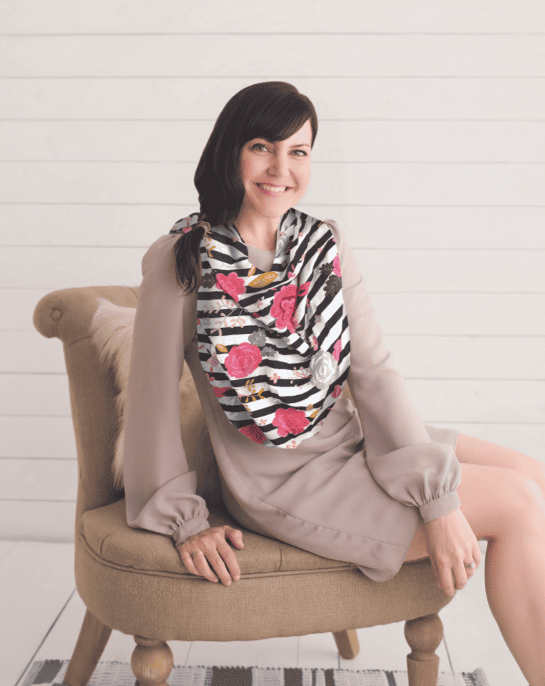 A woman sitting on a chair wearing a Mom Boss™ 4-IN-1 Multi-Use Nursing Cover & Scarf.