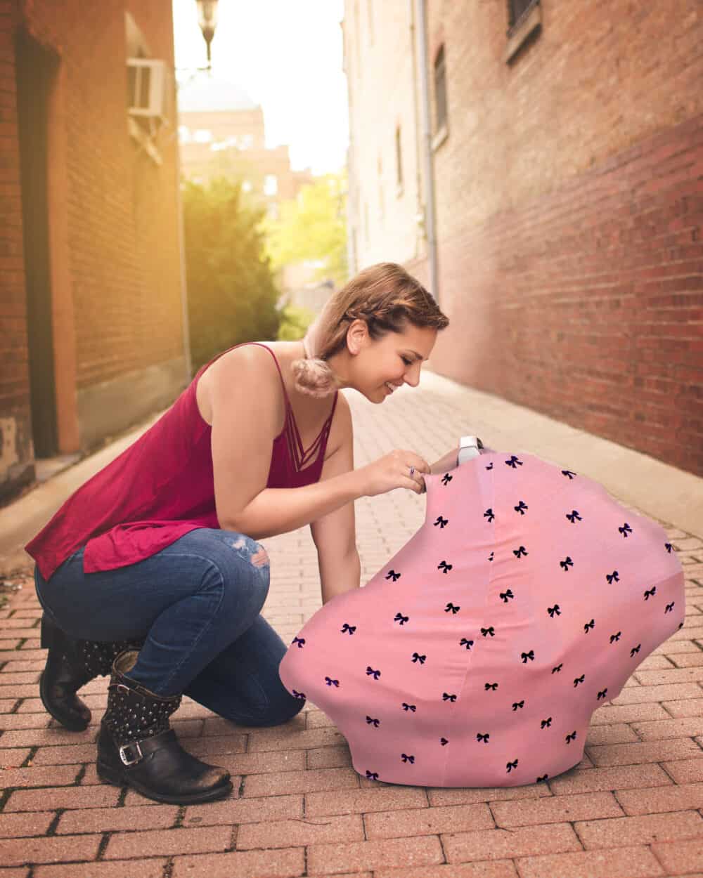 A woman kneeling down next to a Mom Boss™ 4-IN-1 Multi-Use Nursing Cover & Scarf.