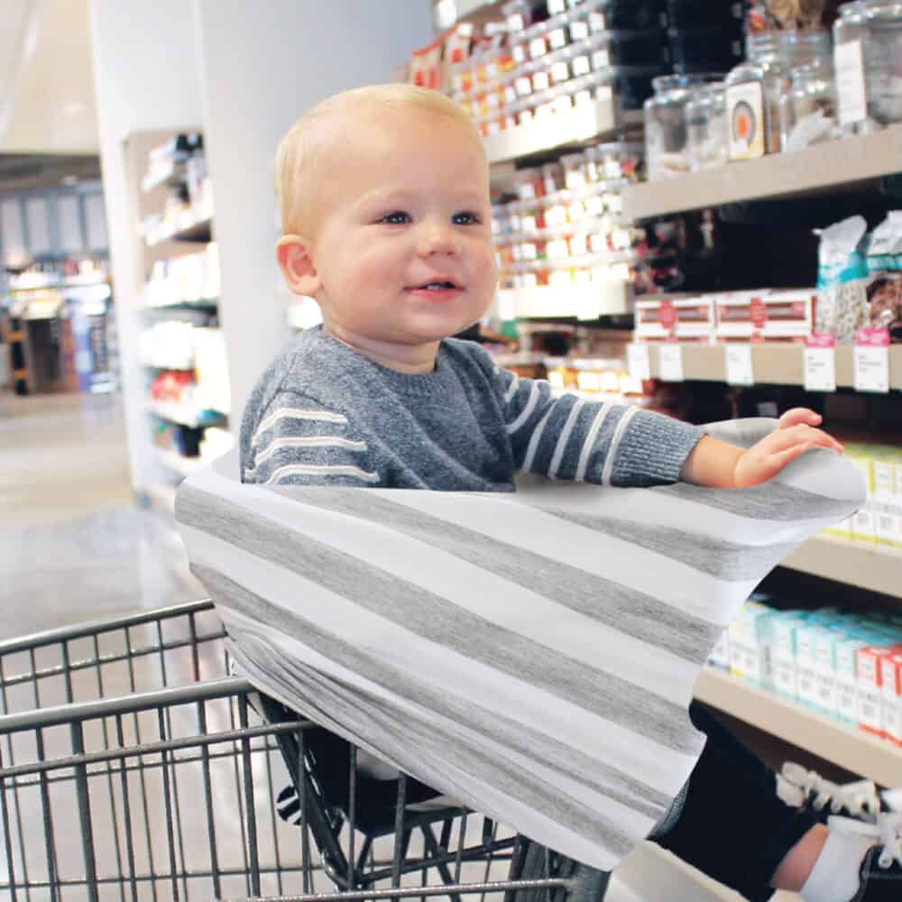 A baby sitting in a Mom Boss™ 4-IN-1 Multi-Use Nursing Cover & Scarf in a grocery store.