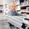 A baby sitting in a Mom Boss™ 4-IN-1 Multi-Use Nursing Cover & Scarf in a grocery store.