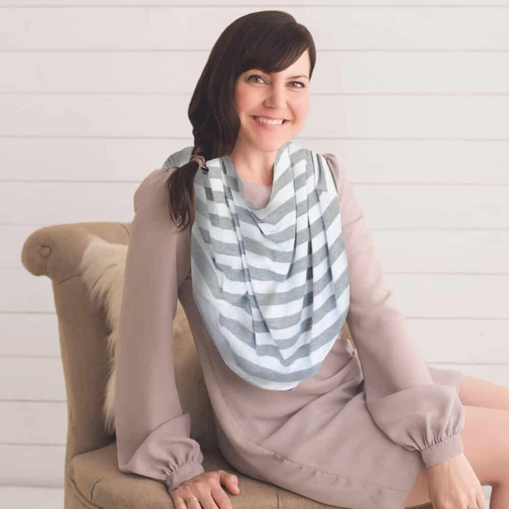 A woman sitting on a chair wearing a Mom Boss™ 4-IN-1 Multi-Use Nursing Cover & Scarf.